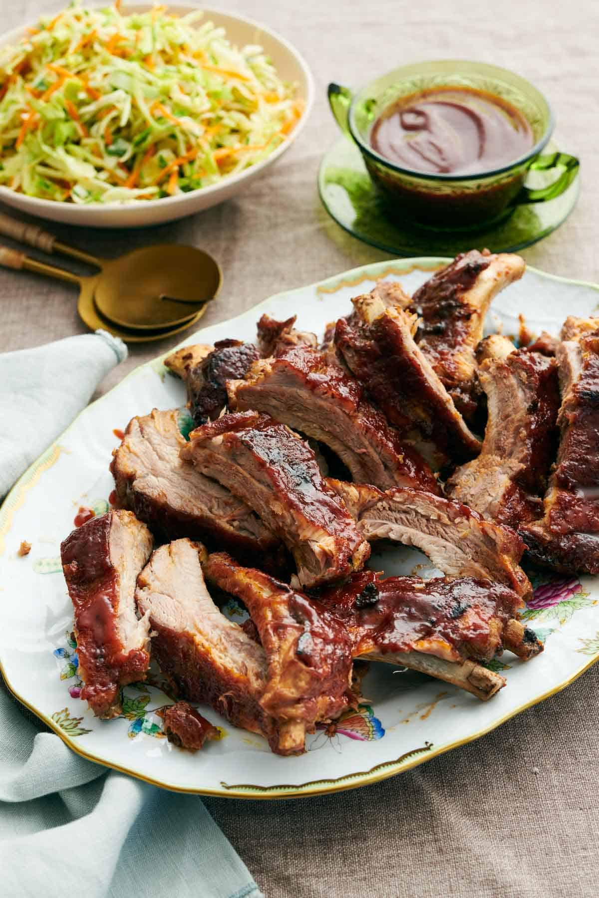 A platter of Instant Pot ribs with a bowl of slaw and barbecue sauce in the background.