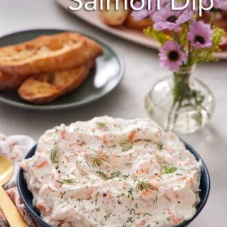 Pinterest graphic of a bowl of smoked salmon dip topped with fresh dill. Bread and flowers in the background.