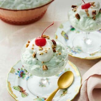 Pinterest graphic of two dessert bowls on plates with Watergate salad topped with whipped cream, pecans, and a maraschino cherry.