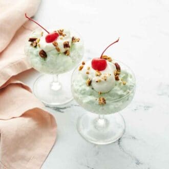 Two servings on Watergate salad with whipped cream, pecans, and maraschino cherries on top. A linen napkin on the side.