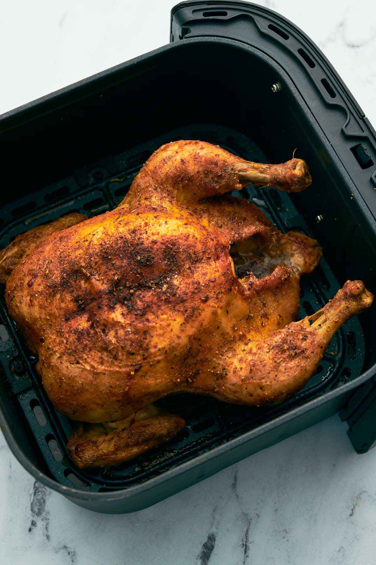 A air fried whole chicken in an air fryer basket.