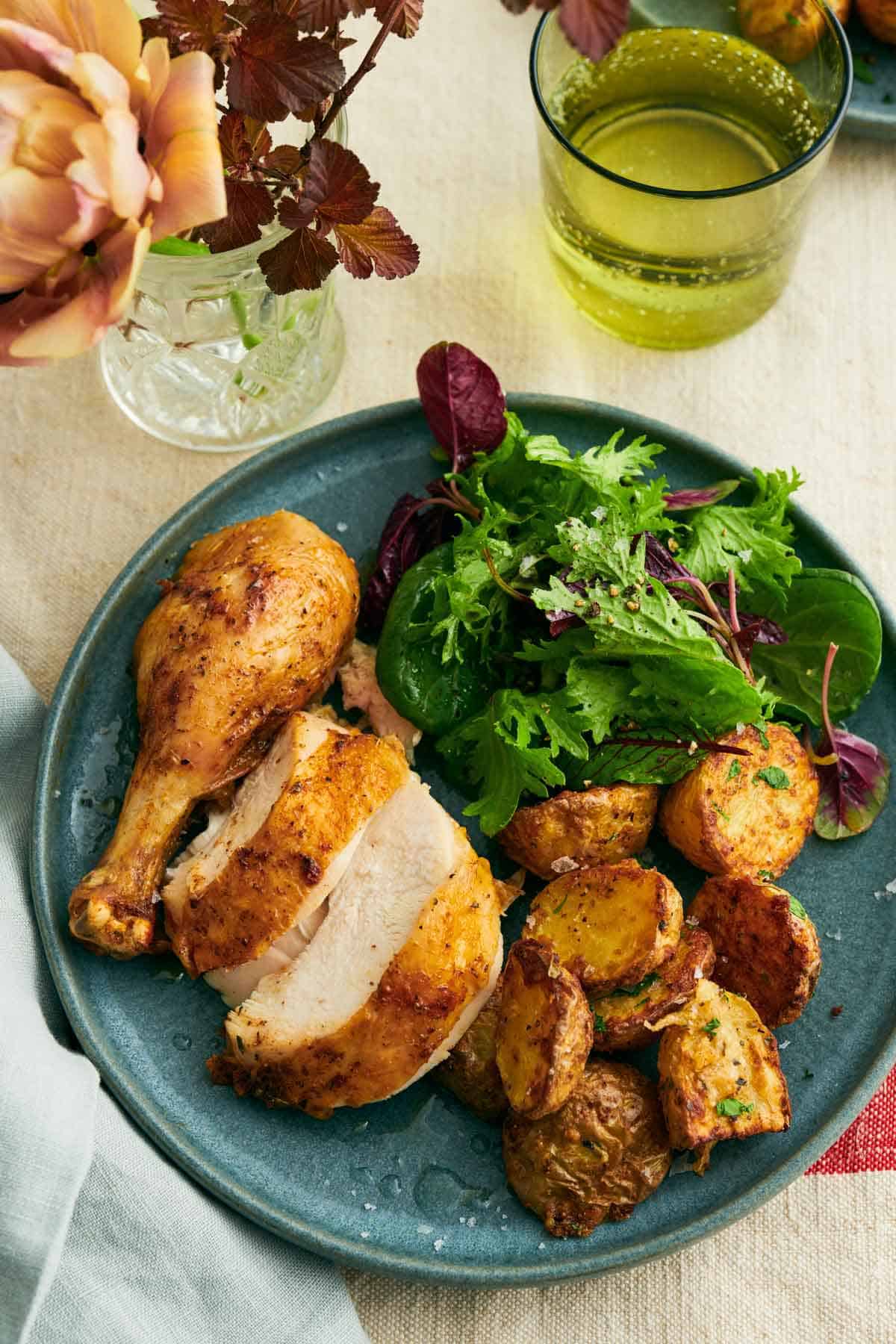 Overhead view of a plate with sliced air fryer chicken, crispy potatoes, and salad. A drink in the background.