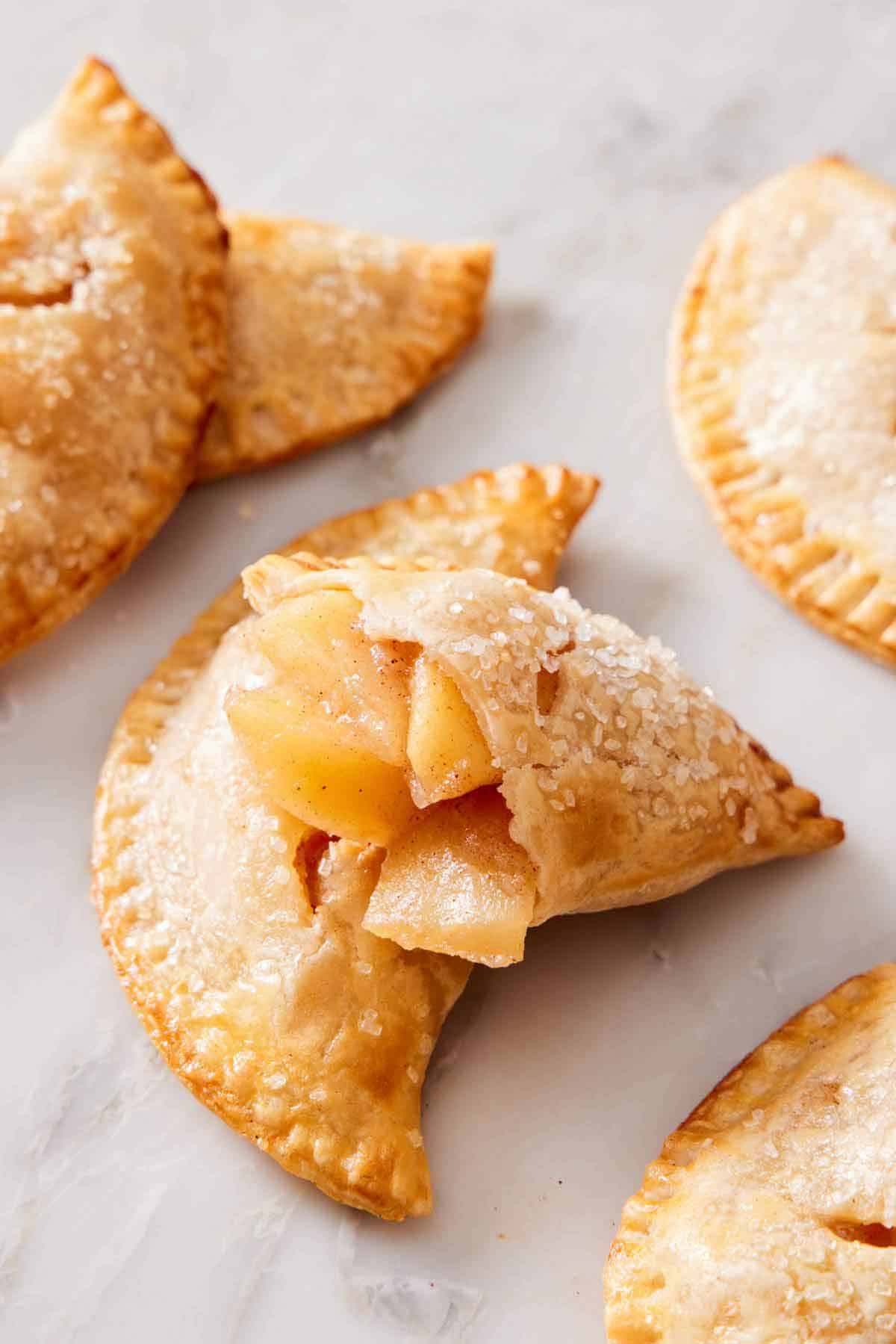 A handheld pie cut opened with apple pie filling. More handheld pies scattered around.