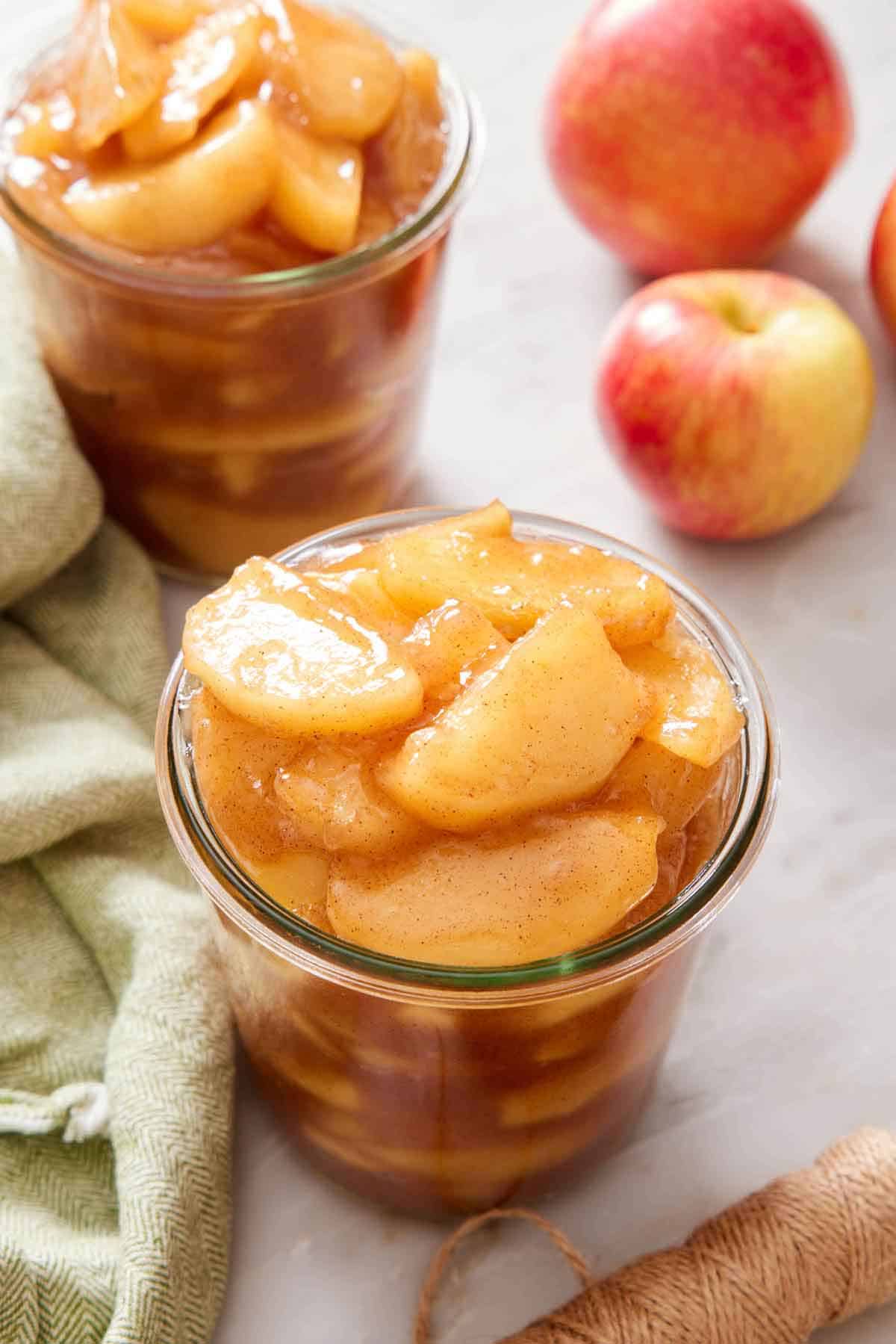 Two jars of apple pie filling. A linen napkin and a couple of apples on the side.