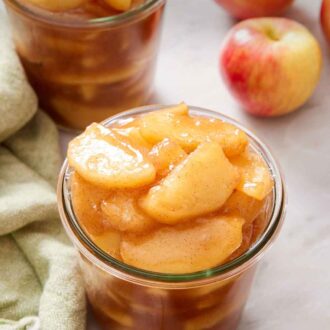 Pinterest graphic of two jars of apple pie filling with some apples in the background.