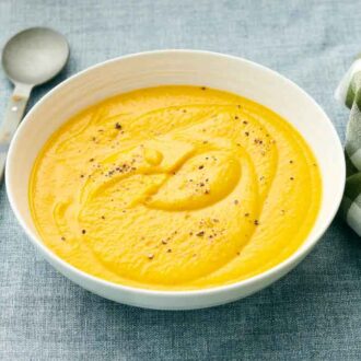 A bowl of carrot soup with freshly cracked pepper on top with a spoon and napkin beside it.