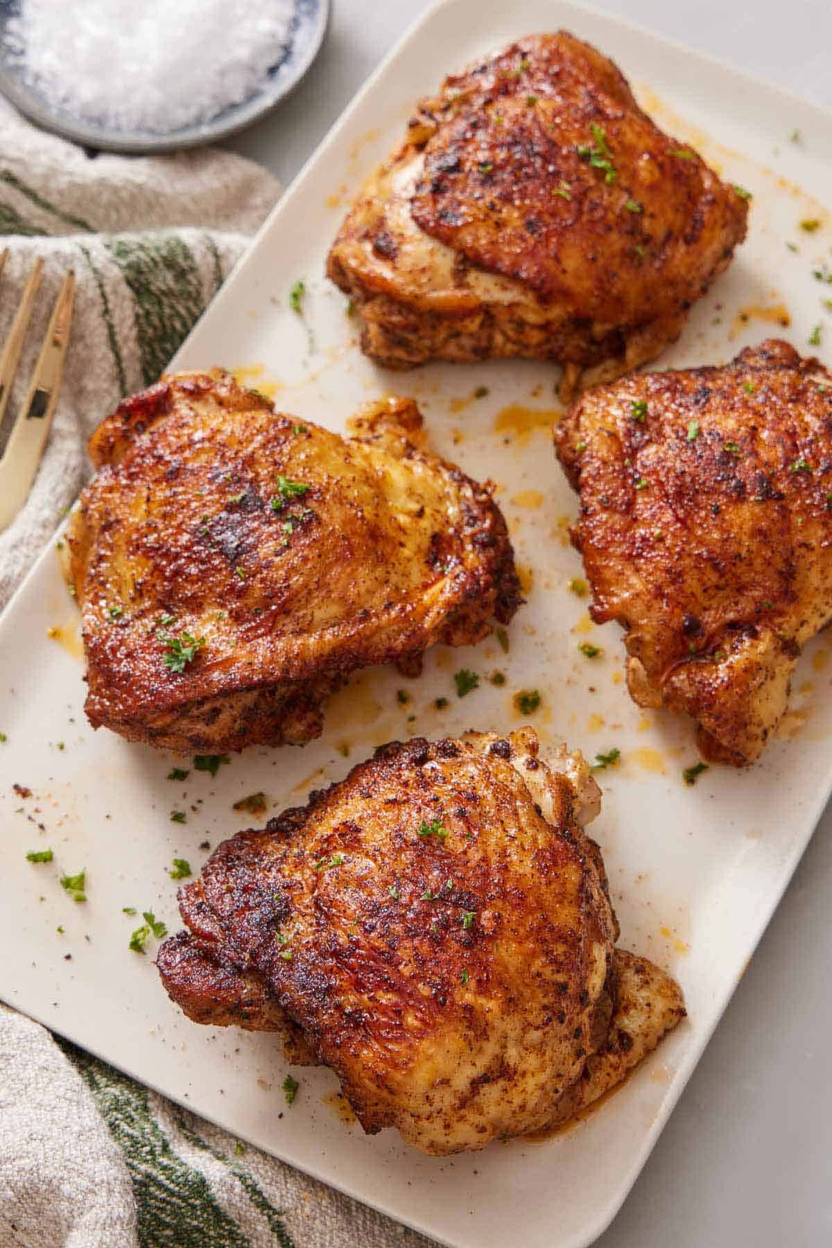 A platter with four Instant Pot chicken thighs topped with chopped parsley.