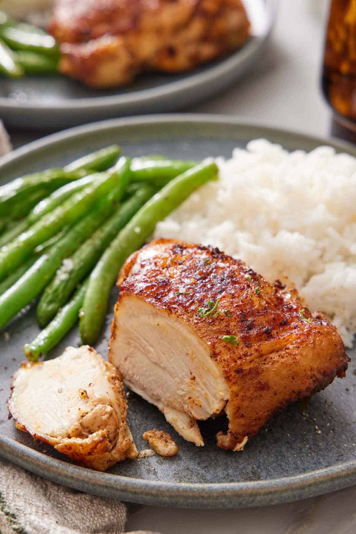 An Instant Pot chicken thigh cut on a plate with rice and green beans.