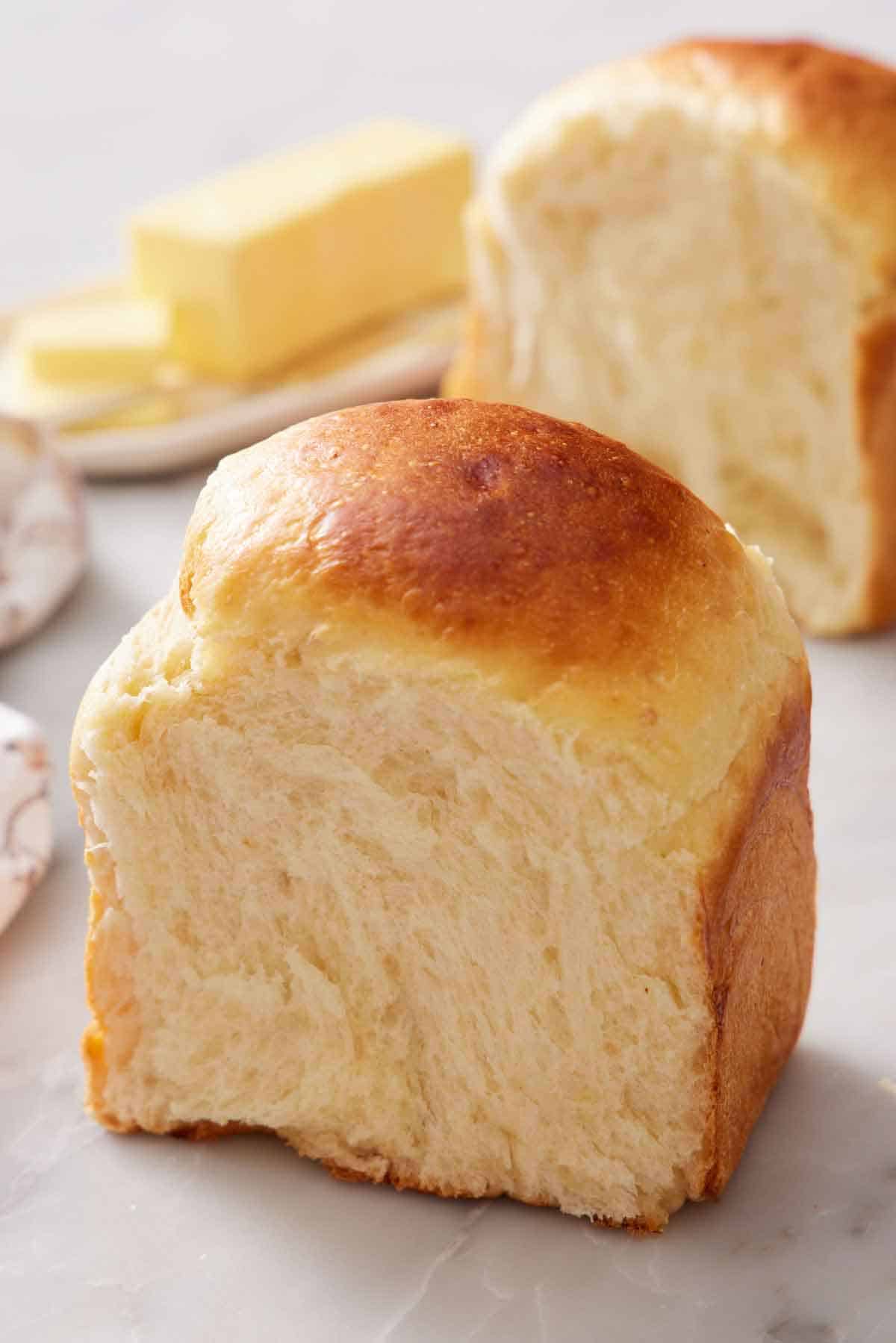 A piece of milk bread cut and standing upright. Another piece in the background with butter on the side.