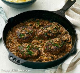 Pinterest graphic of a cast iron skillet of salisbury steaks with a bowl of mashed potatoes in the back.