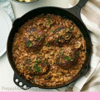 Pinterest graphic of an overhead of a cast iron skillet of salisbury steaks with a bowl of mashed potatoes on the side.
