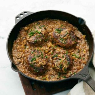 A skillet with four salisbury steaks and sauce.
