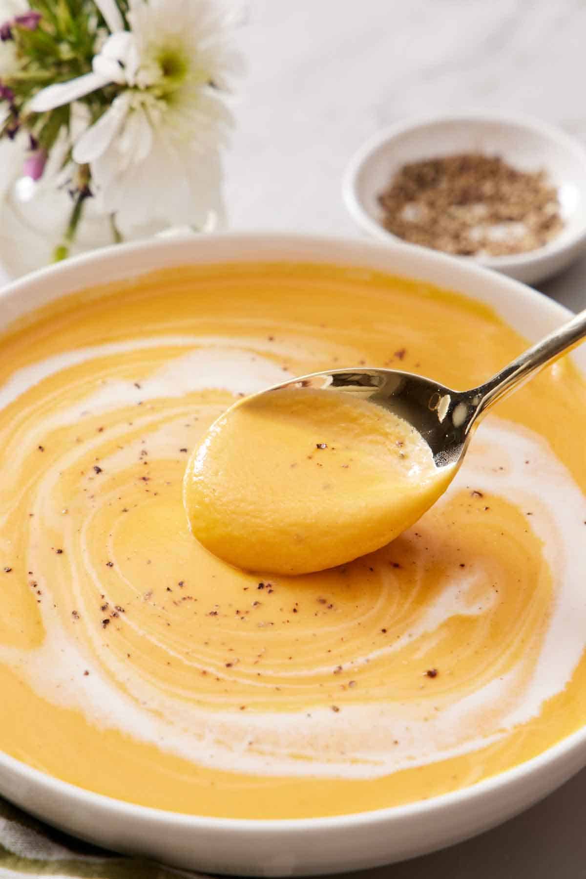 A bowl of creamy sweet potato soup with a spoonful lifted up.