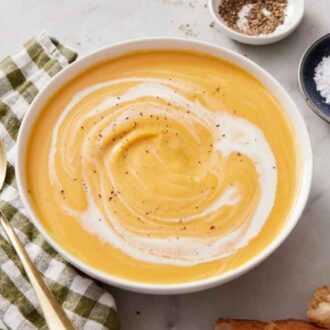 A bowl of sweet potato soup with cream and black pepper on top. A bowl of salt, pepper, and spoon on the side.