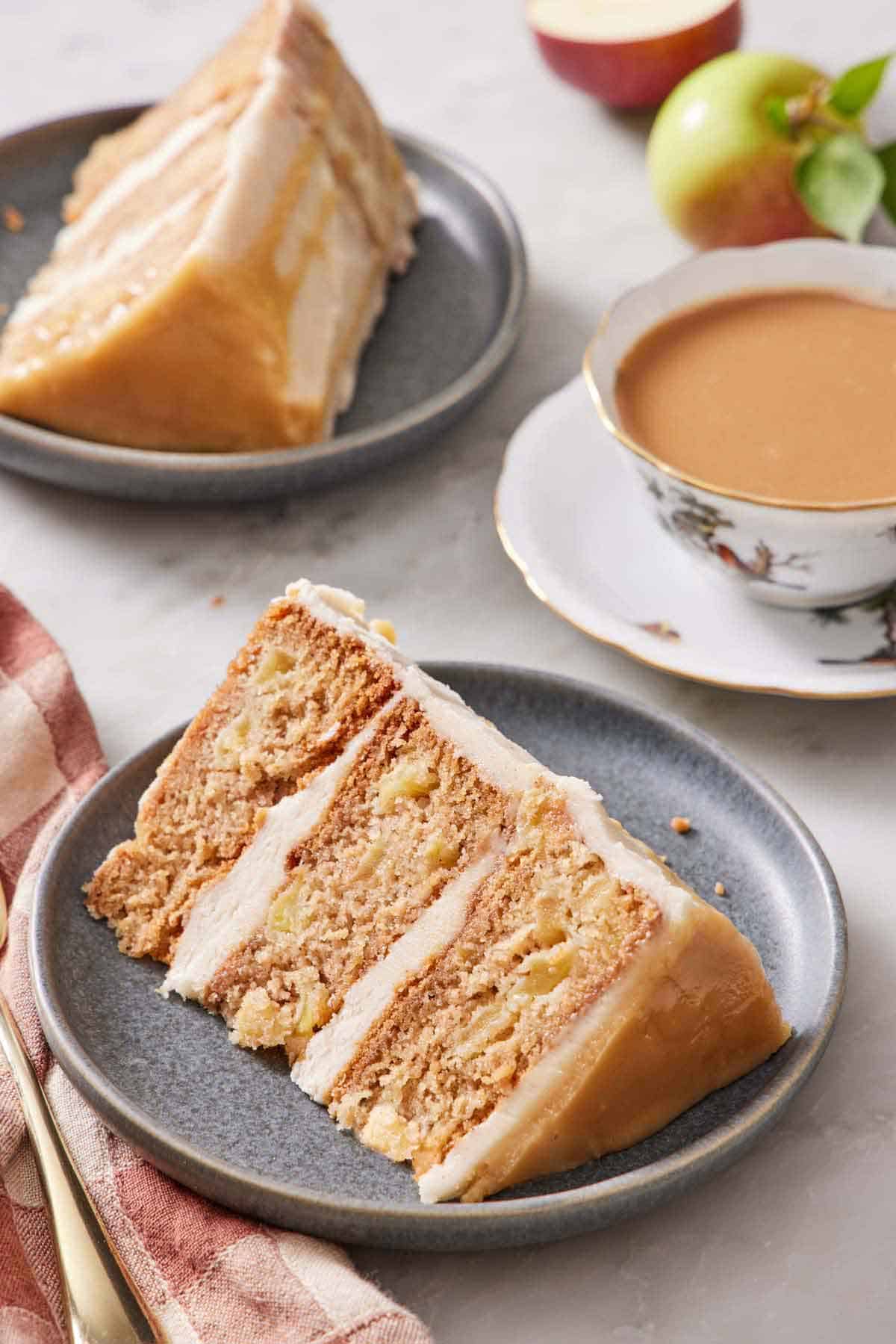 A plate with a slice of caramel apple cake on its side. Another slice in the background along with a cup of coffee.
