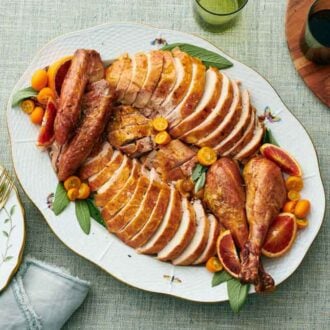 Overhead view of a platter of a carved turkey. Drinks, plates, and forks on the side.