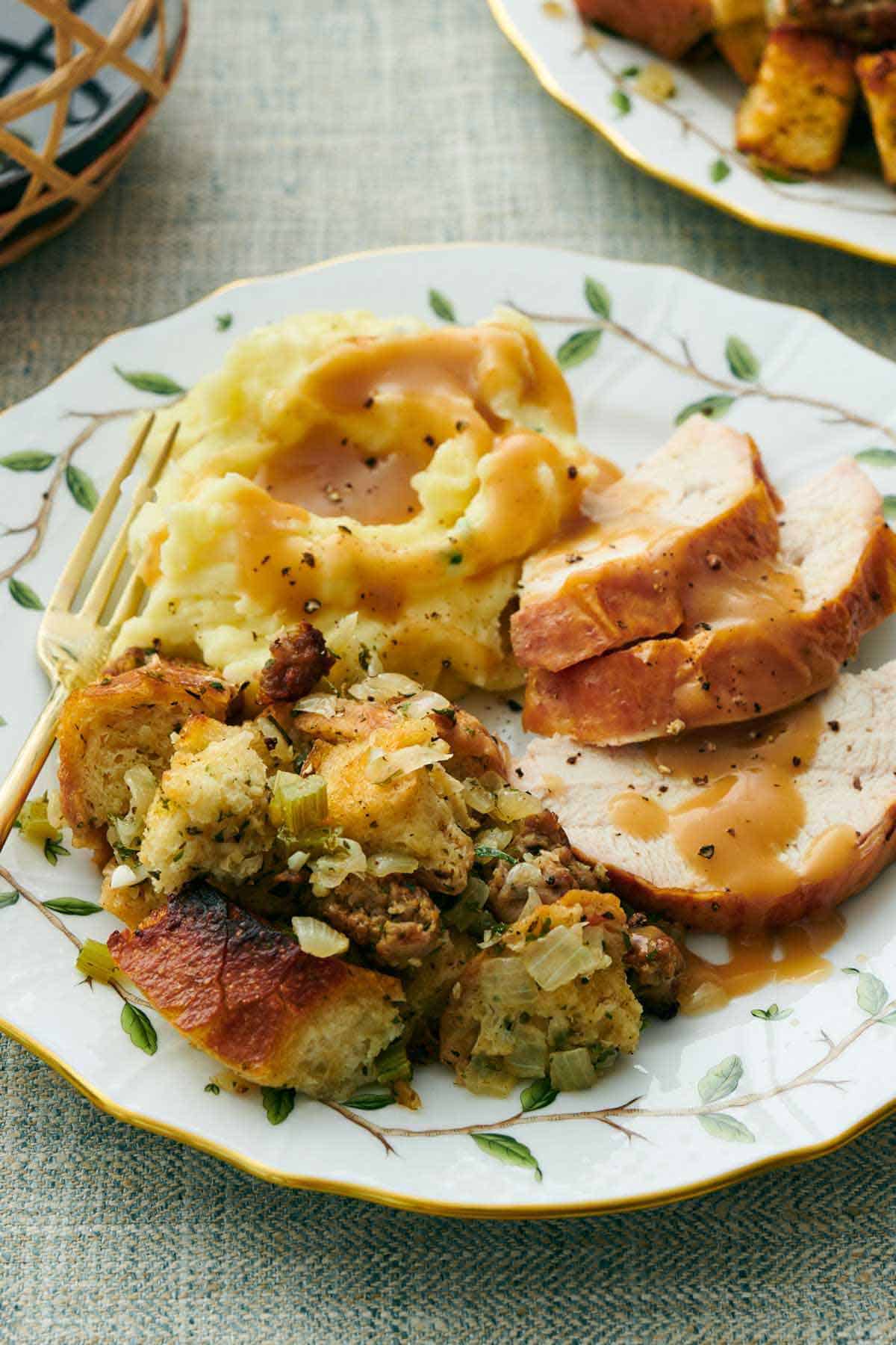 A plate with sausage stuffing, sliced turkey, and mashed potatoes with gravy on top.