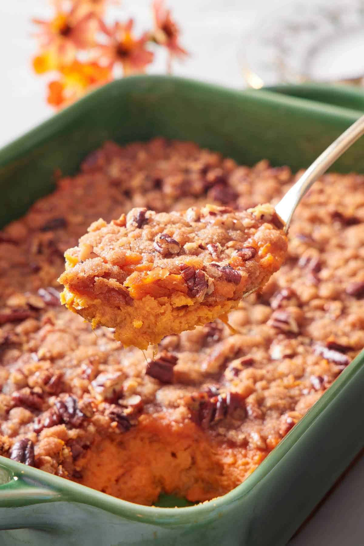 A spoonful of sweet potato casserole lifted from the green baking dish.