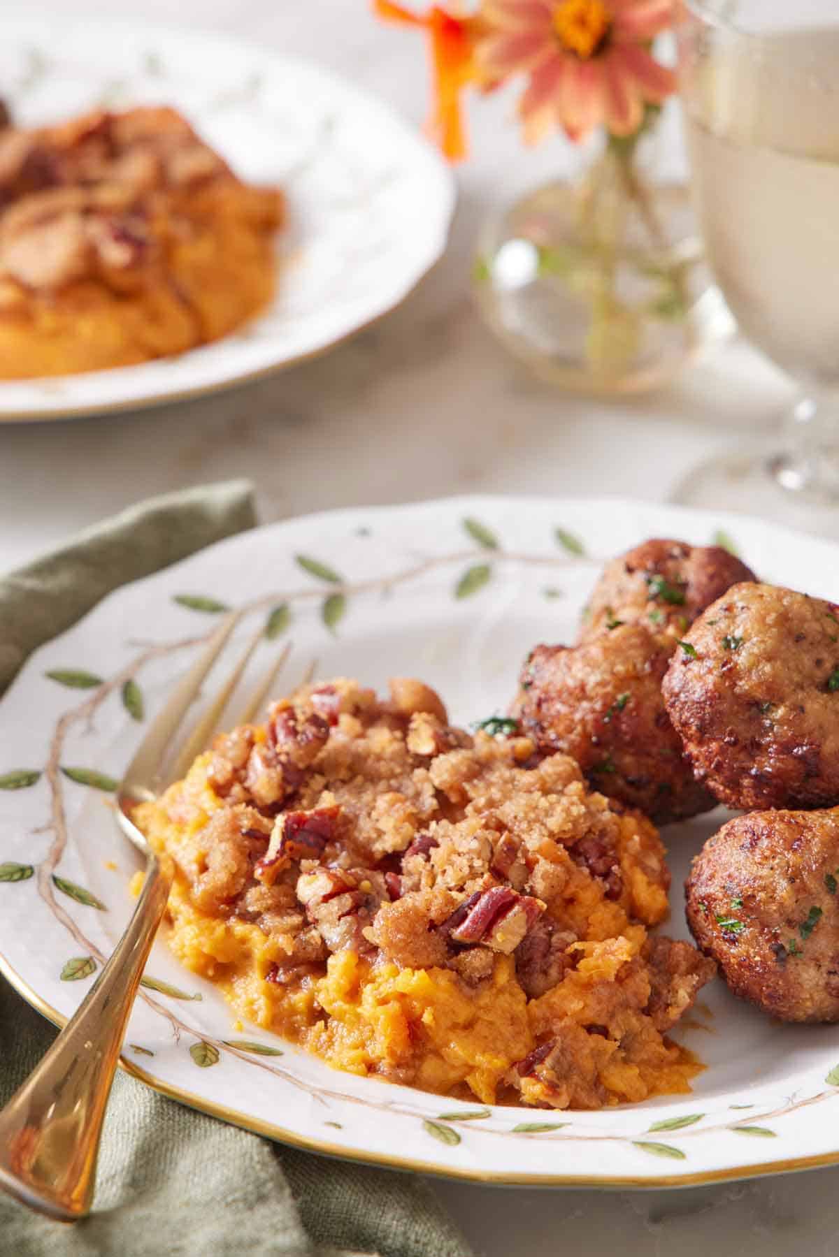 A close up view of a serving of sweet potato casserole on a plate with some meatballs beside it and a fork.