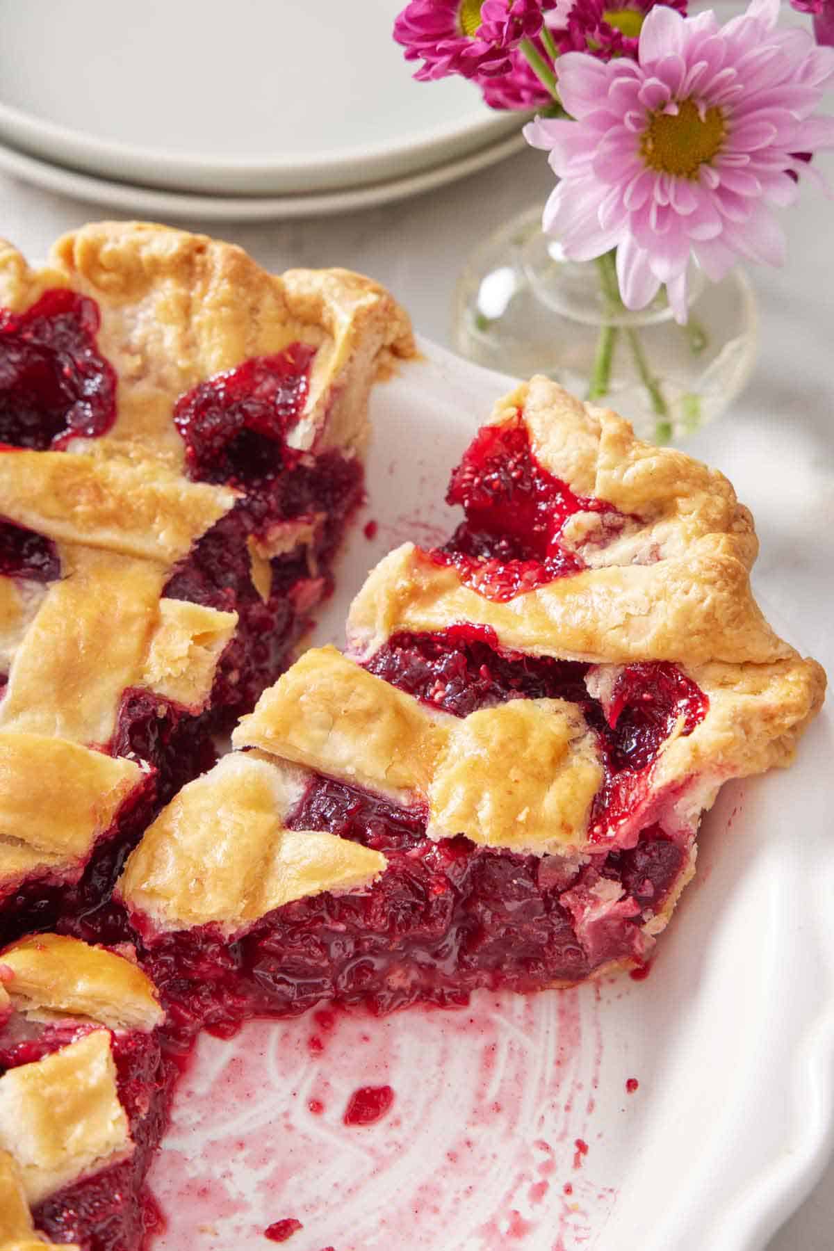 A close up view of a cut slice of cranberry pie in the baking dish. Flowers in the background.