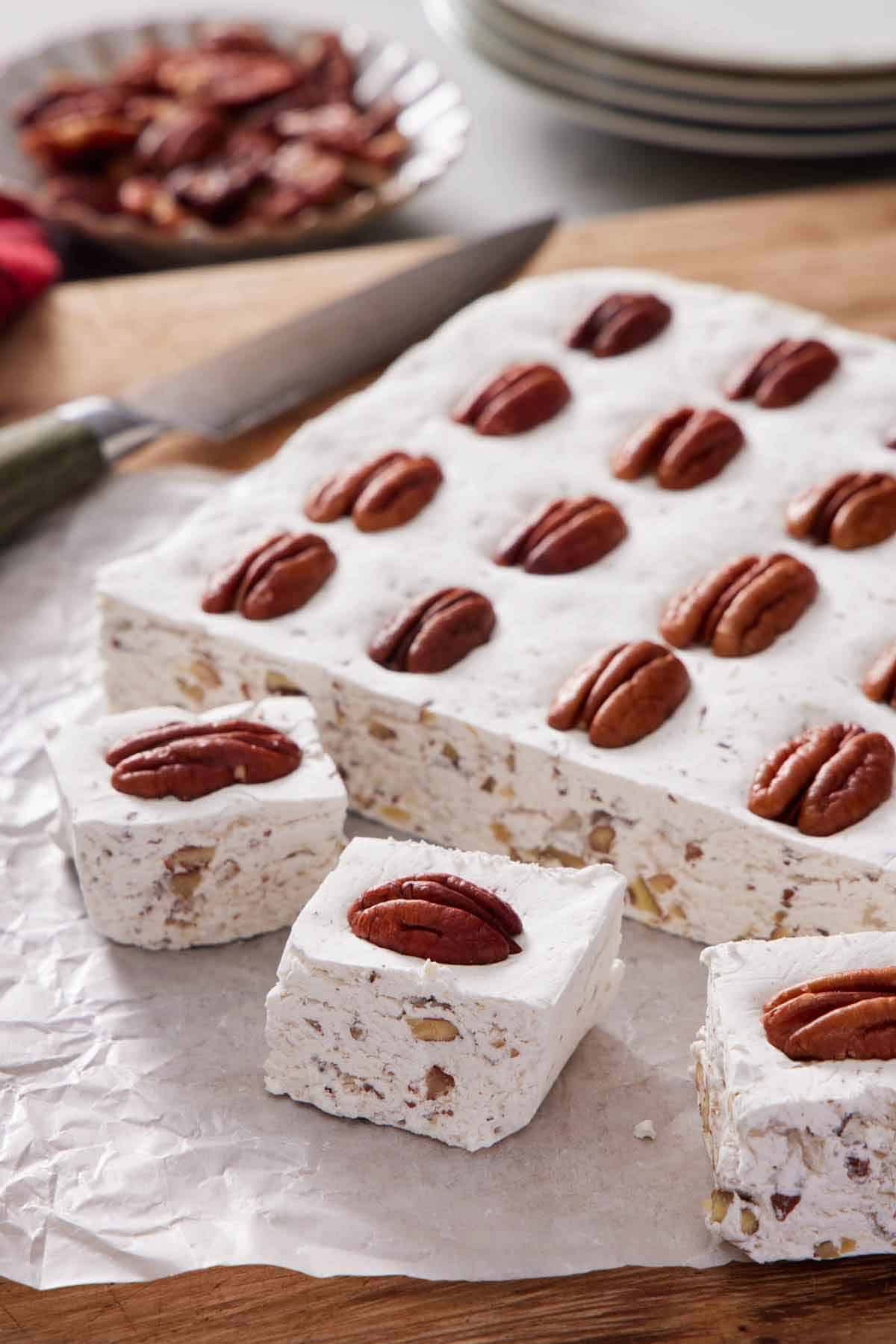 Three pieces of divinity candy cut from a slab with pecans on top.