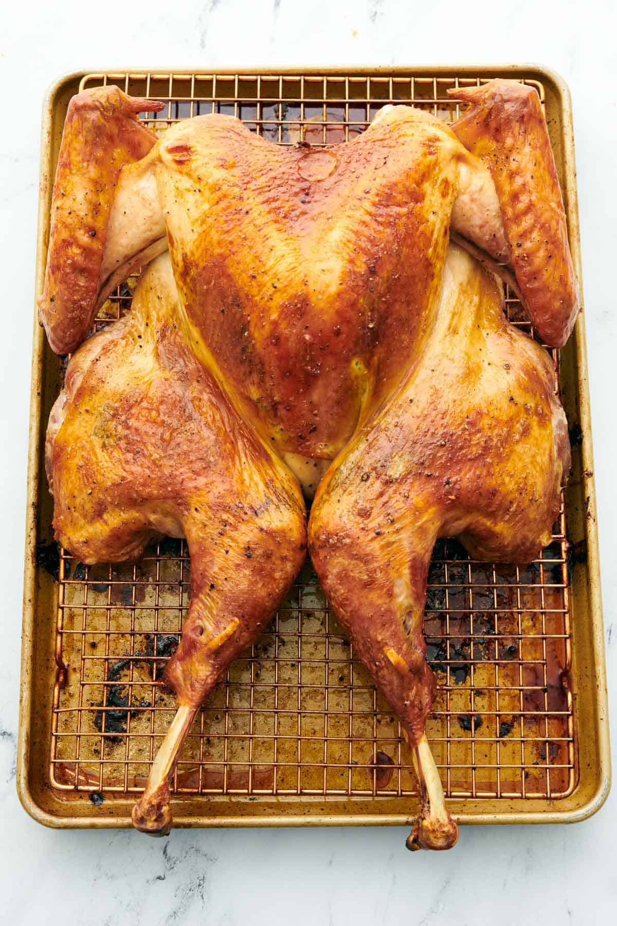 A spatchcock turkey on a sheet pan with a cooling rack.