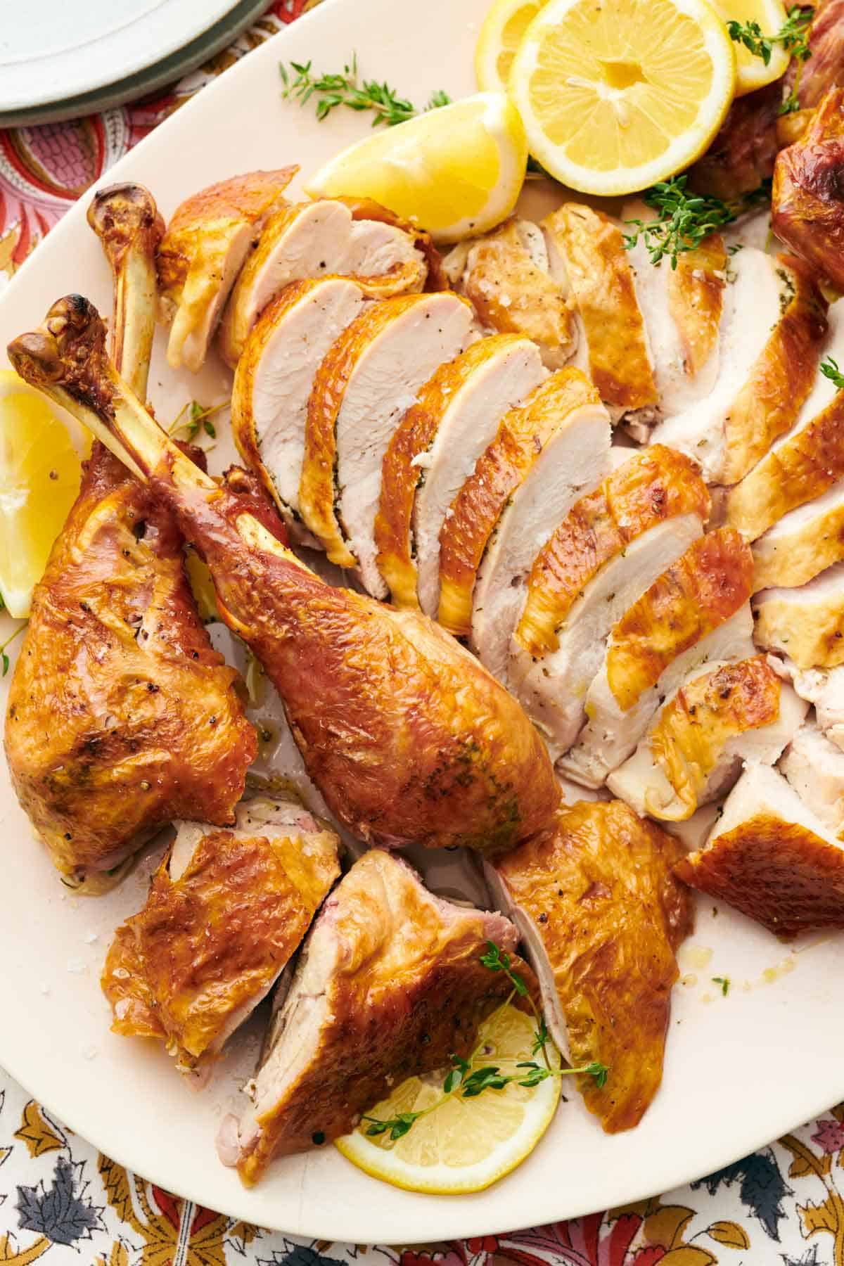 A close up view of a sliced spatchcock turkey with cut lemons and fresh herbs.