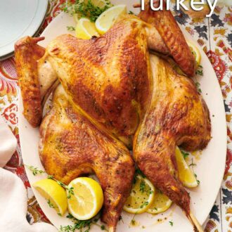Pinterest graphic of a platter with a spatchcock turkey surrounded by fresh herbs and lemons. A bowl of cranberry sauce and plates off to the side.