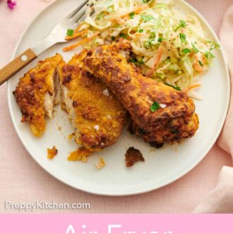 Pinterest graphic of a plate with two pieces of air fryer fried chicken with a piece cut along with coleslaw.