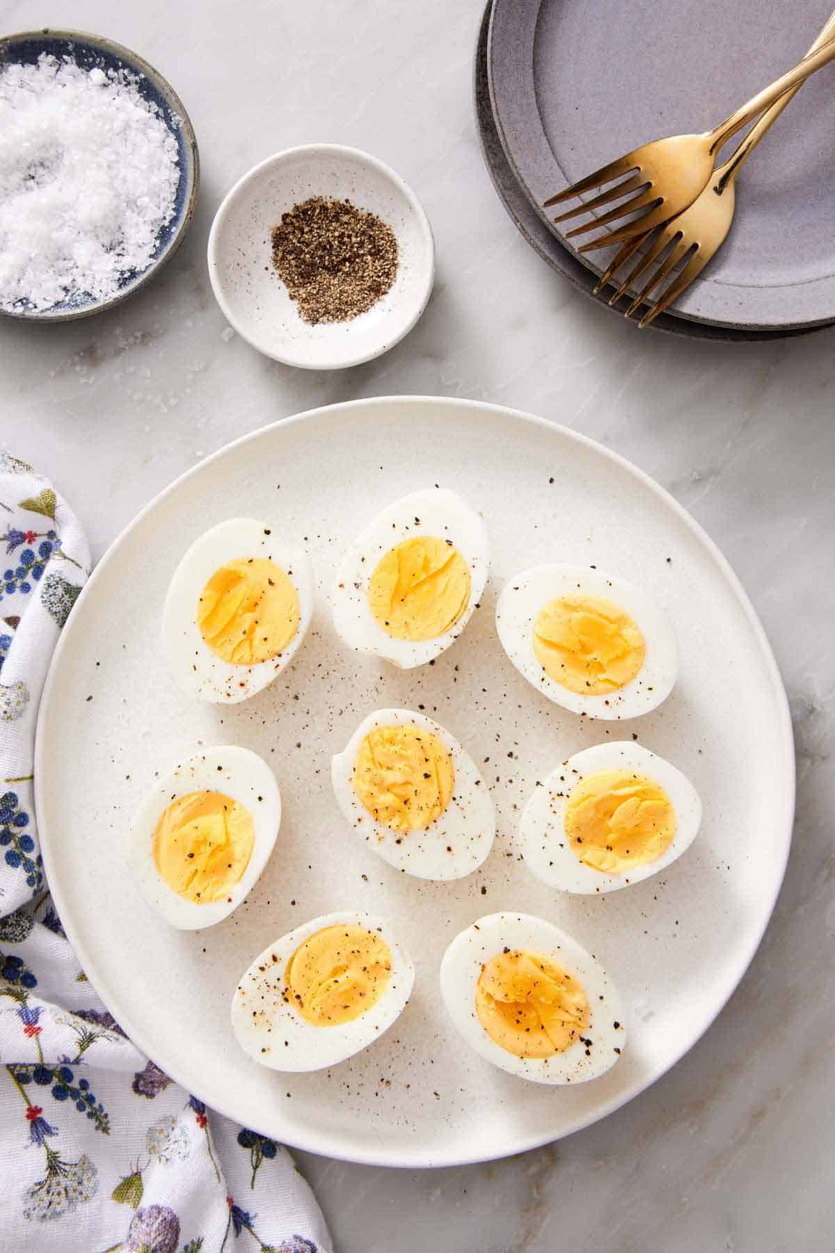 Overhead view of a platter of air fryer hard boiled eggs cut in half topped with pepper. A bowl of salt and pepper in the back along with plates and forks.