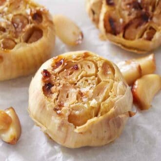 A close up view of air fryer roasted garlic with salt sprinkled on top. A bowl of salt on the side along with loose cloves.
