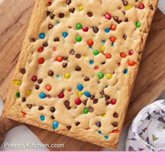 Pinterest graphic of an uncut slab of M&M cookie bars on a wooden serving board.