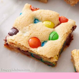 Pinterest graphic of a piece of M&M cookie bar on a marble surface.