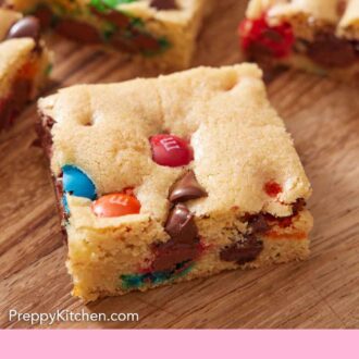 Pinterest graphic of cut M&M cookie bars on a wooden serving board.