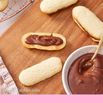 Pinterest graphic of a Milano cookie in the process of being assembled with melted chocolate spread onto a cookie.
