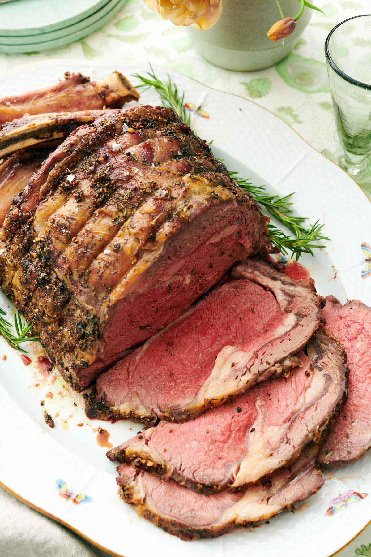 A prime rib on a serving platter with four slices cut in front.