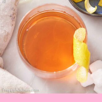 Pinterest graphic of an overhead view of a glass of Sazerac with a lemon zest garnish on the rim.