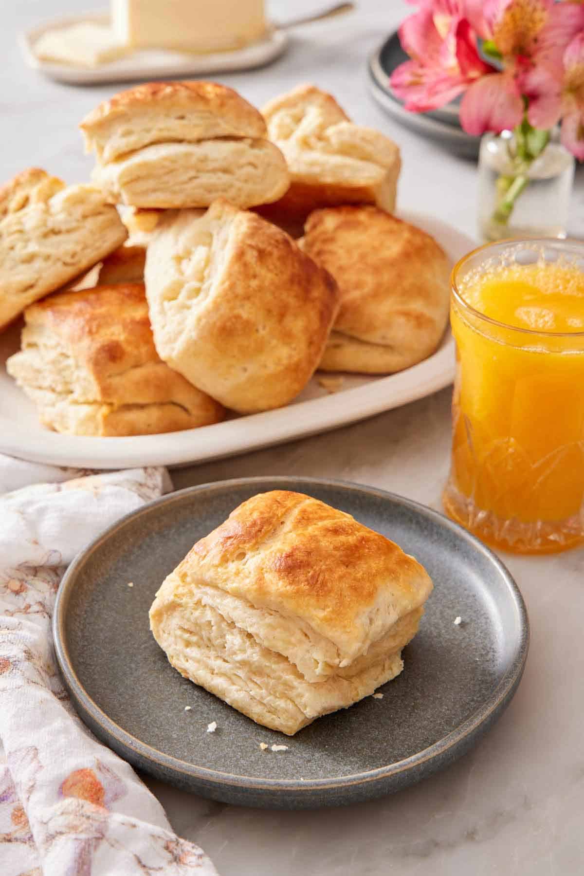 A plate with a sourdough biscuit with an orange juice and platter of more biscuits in the background.