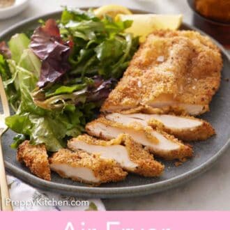 Pinterest graphic of a plate with an air fryer chicken cutlet with half of it sliced along with some mixed greens.