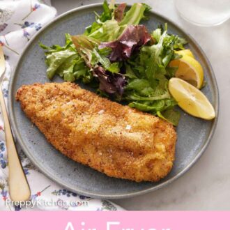 Pinterest graphic of a plate with an air fryer chicken cutlet, mixed greens, and lemon wedges.