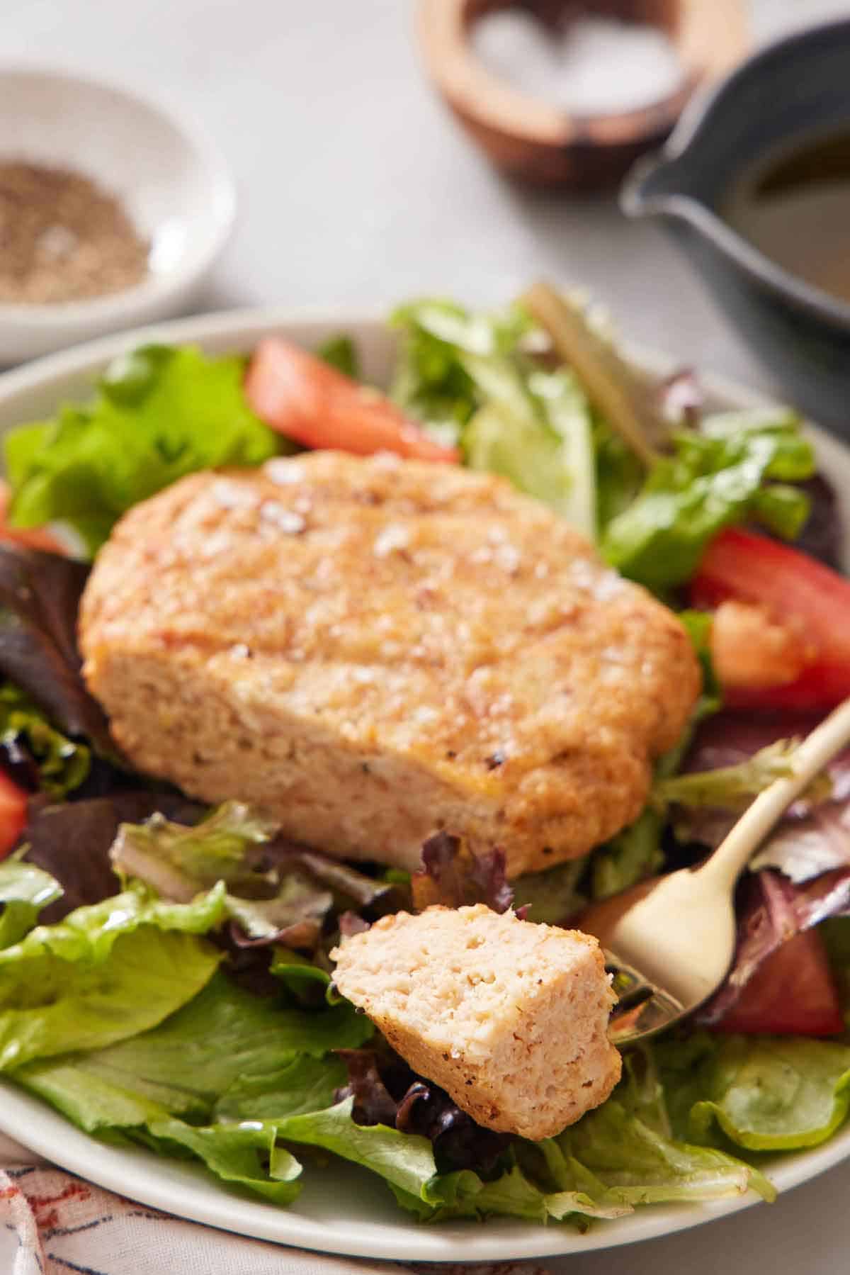 A plate with an air fryer chicken patty with a bite on a fork, over a bed of lettuce.