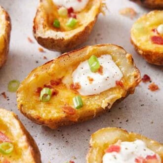 Multiple air fryer potato skins with crumbled bacon, green onions, and sour cream.