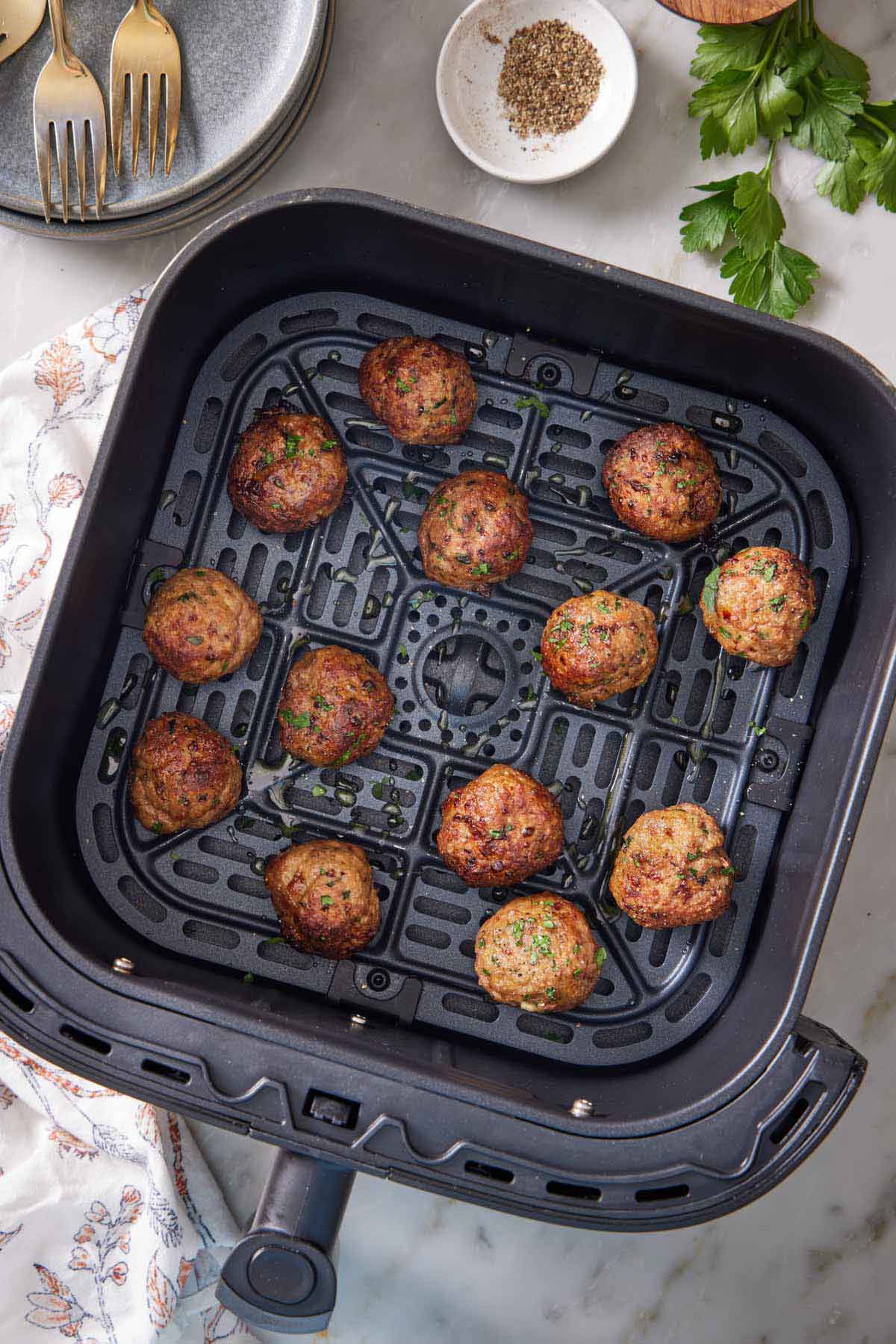 Overhead view of air fryer turkey meatballs garnished with parsley in an air fryer basket.
