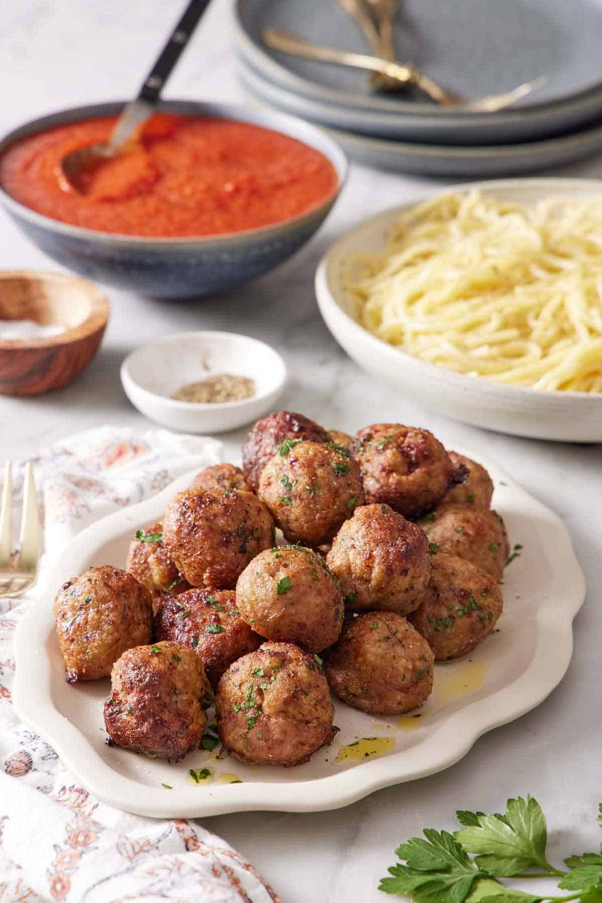A platter of air fryer turkey meatballs with sauce and noodles in the back along with salt and pepper and plates.