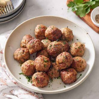 A bowl of air fryer turkey meatballs with chopped parsley. Pepper, parsley, and some plates and forks in the background.