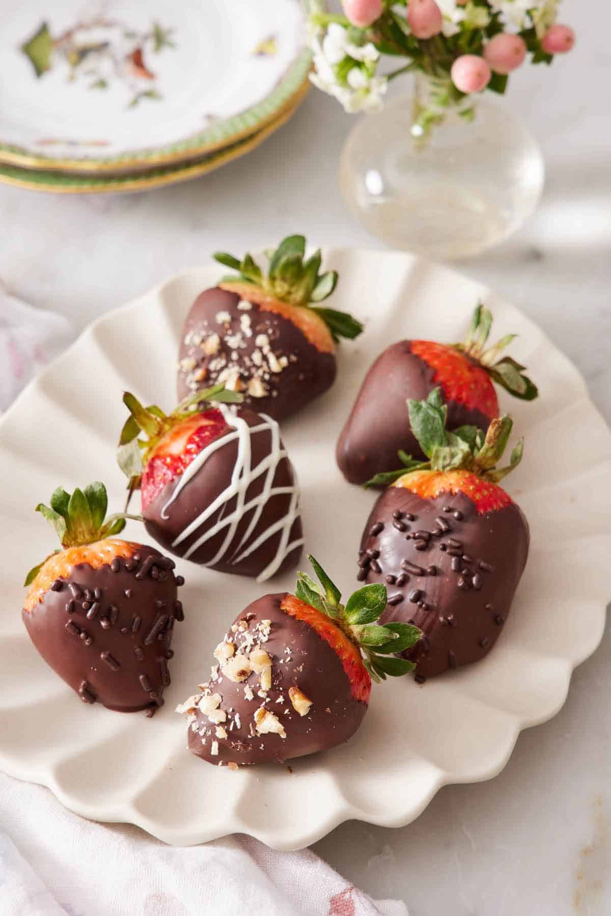 A scalloped platter of chocolate covered strawberries with different patterns and toppings.