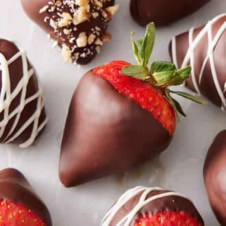 Multiple chocolate covered strawberries with different designs on a marble surface.