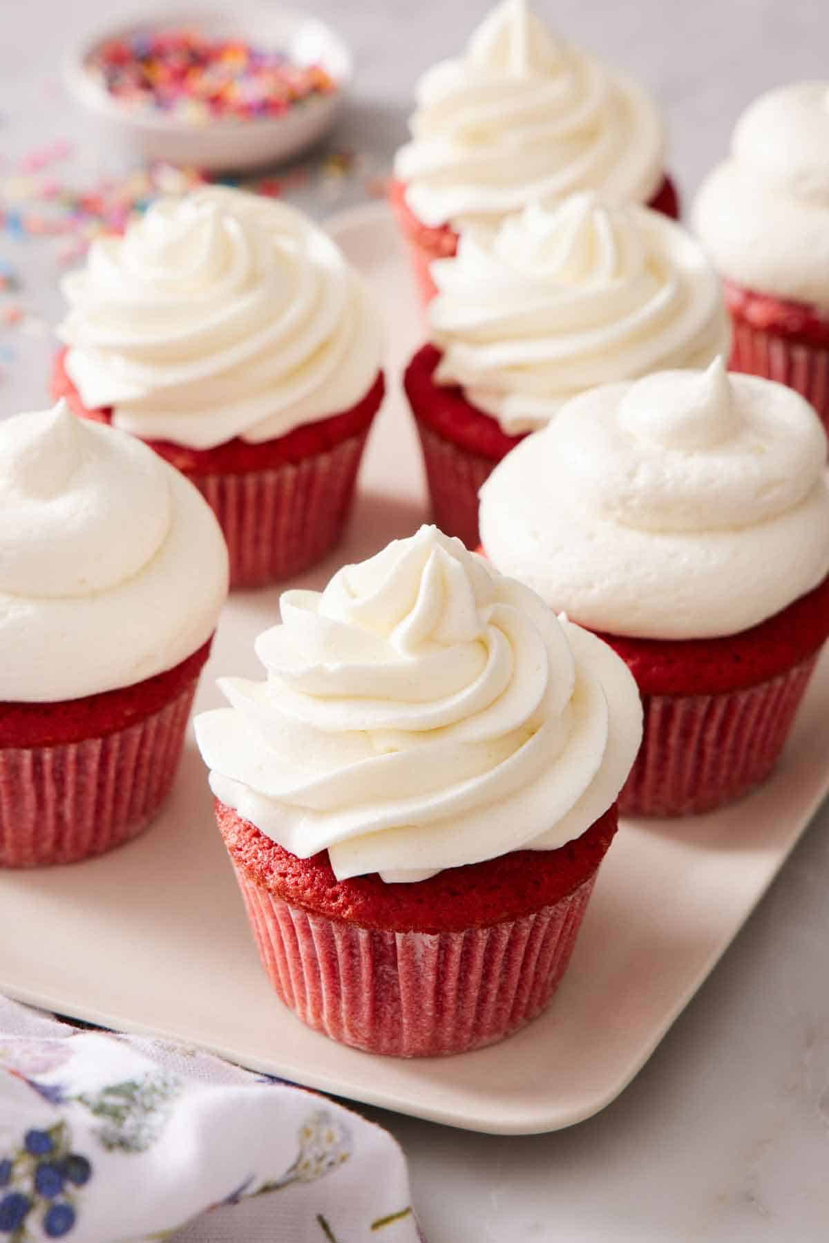 A platter of seven red velvet cupcakes with ermine frosting.