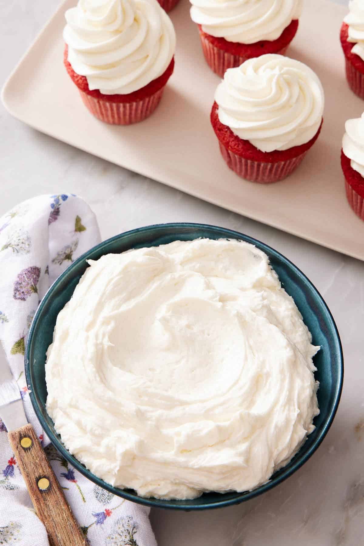 Overhead view of a bowl of ermine frosting with frosted cupcakes on the side.