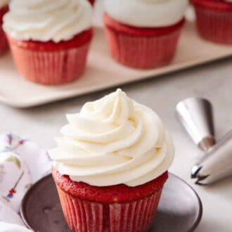 Pinterest graphic of a red velvet cupcake with ermine frosting. More frosted cupcakes in the background.